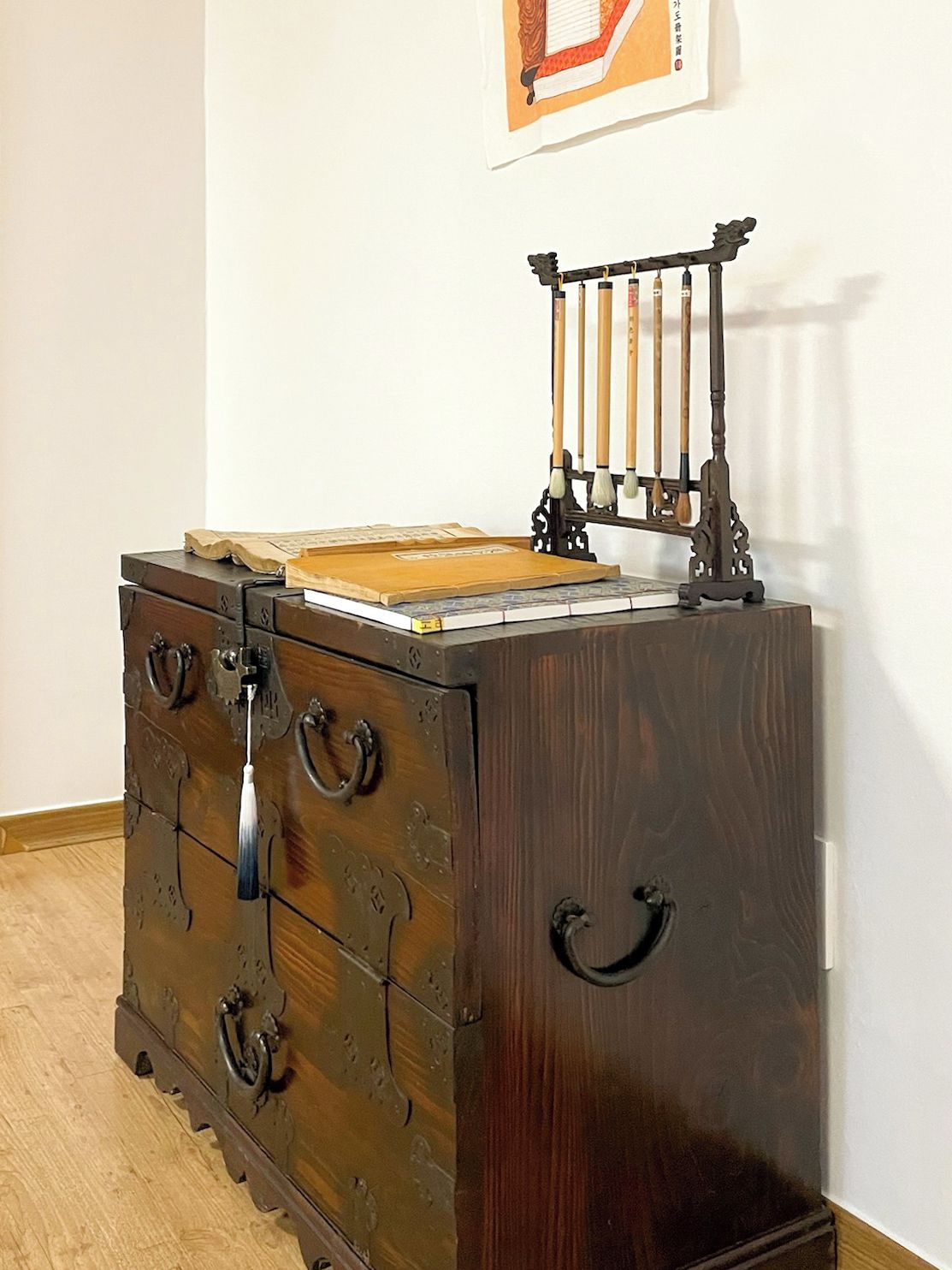 A wooden dresser with multiple drawers and a small shelf, a framed picture on the wall, and a traditional Chinese instrument on top.