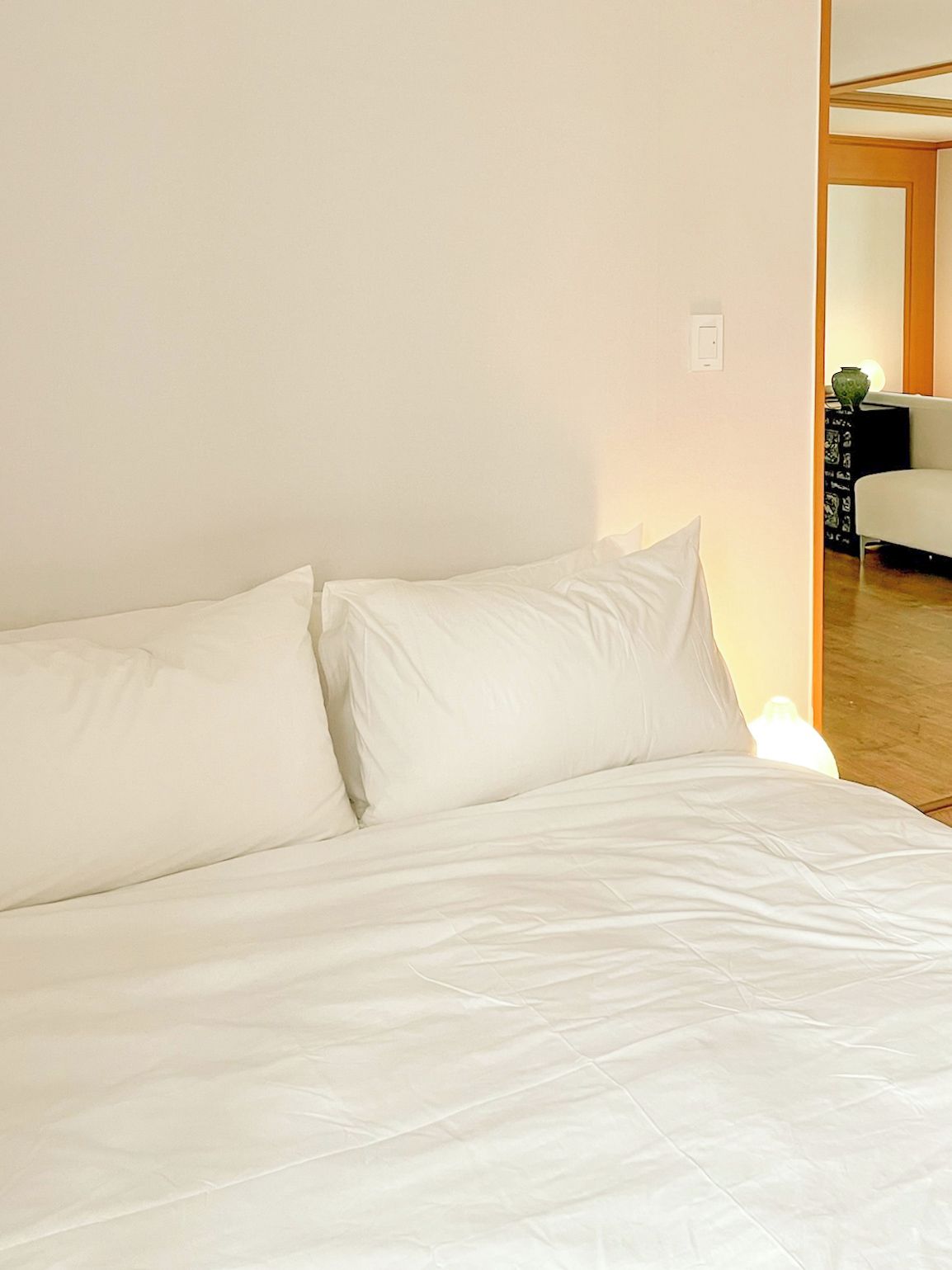 A bed with white bedding in a room with plain walls.