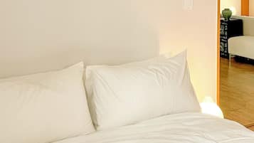 A bed with white bedding in a room with plain walls.