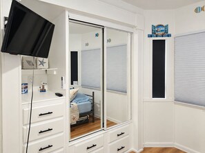 A bedroom with a sliding closet door, a bed with a blue bedspread, a dresser with drawers, a mounted television, and a wall decoration. - Turtle Nest in the Keys - Cozy RV Retreat in Key Largo - Golf Cart Included (Key Largo)