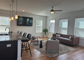 A modern living room with a kitchen island, seating area, and a ceiling fan. - Spacious 3BR Downtown Near VCU With Private Rooftop Patio & Free Parking (Richmond)