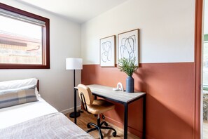A hotel room with a bed, a desk, a chair, a lamp, and two framed artworks on the wall. - Spacious 2BR Near Colorado School of Mines | Workspaces + Patio (Golden)