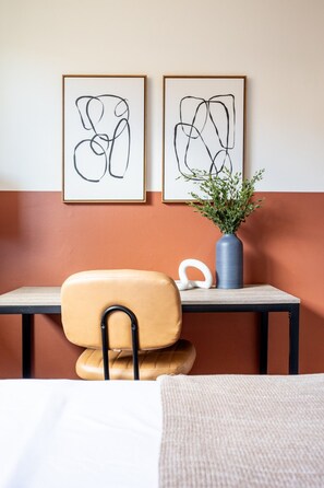 Une pièce comprenant un lit, une chaise, une table et deux œuvres d’art abstrait accrochées au mur.