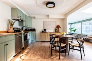 Une cuisine avec des meubles de rangement verts, un plan de travail en bois et un coin repas comprenant une table ronde et des chaises.