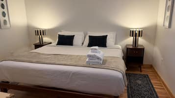 Habitación de hotel con una cama grande, dos mesitas de noche con lámparas, un tapete oscuro y un cuadro colgado en la pared.