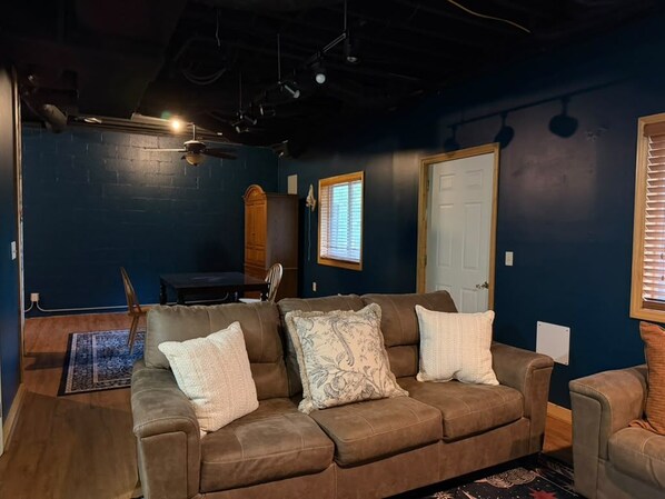 A room with a brown leather couch, a wooden door, and a window with blinds.