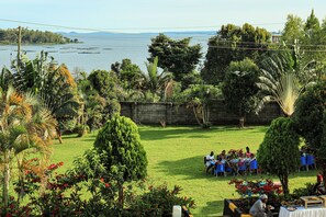 An outdoor dining area with tables set up for guests, surrounded by lush greenery and a view of the water.