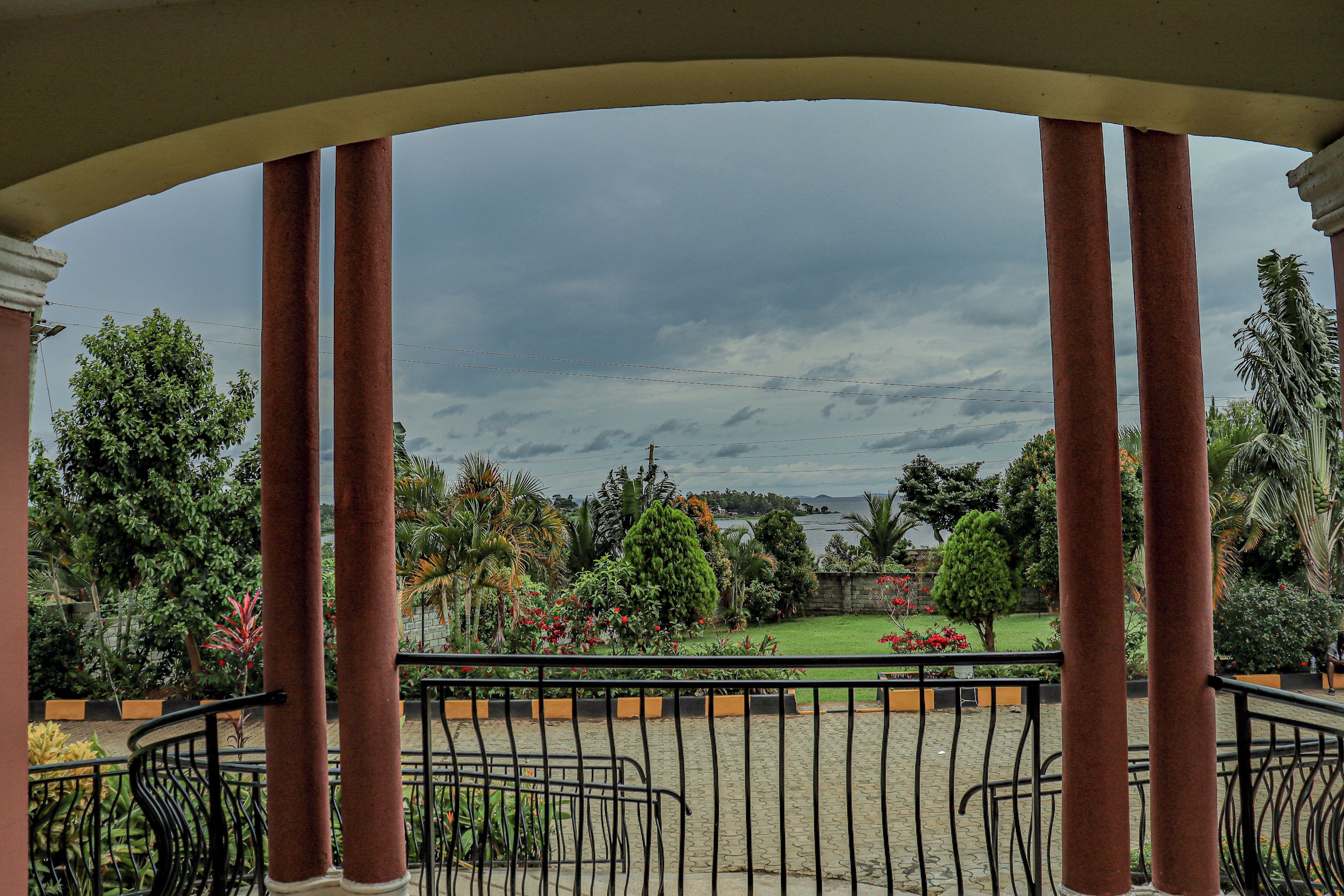 A covered outdoor area with a view of a landscaped garden and a body of water.