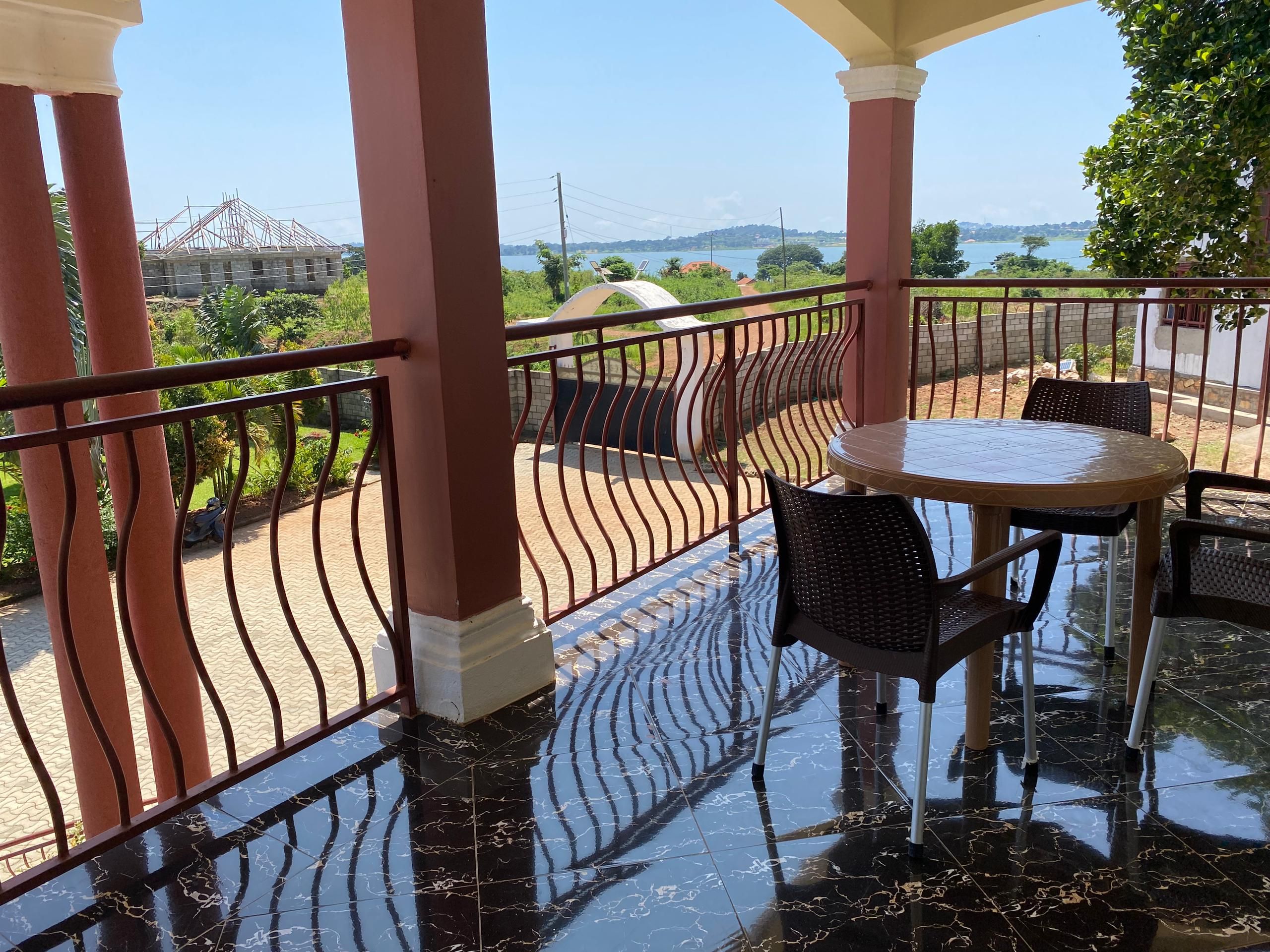 A balcony with a glass table and chairs, a metal railing, and a view of a construction site and water body.