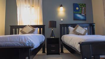 A hotel room with two beds, a nightstand, a lamp, a painting, and a window with curtains.