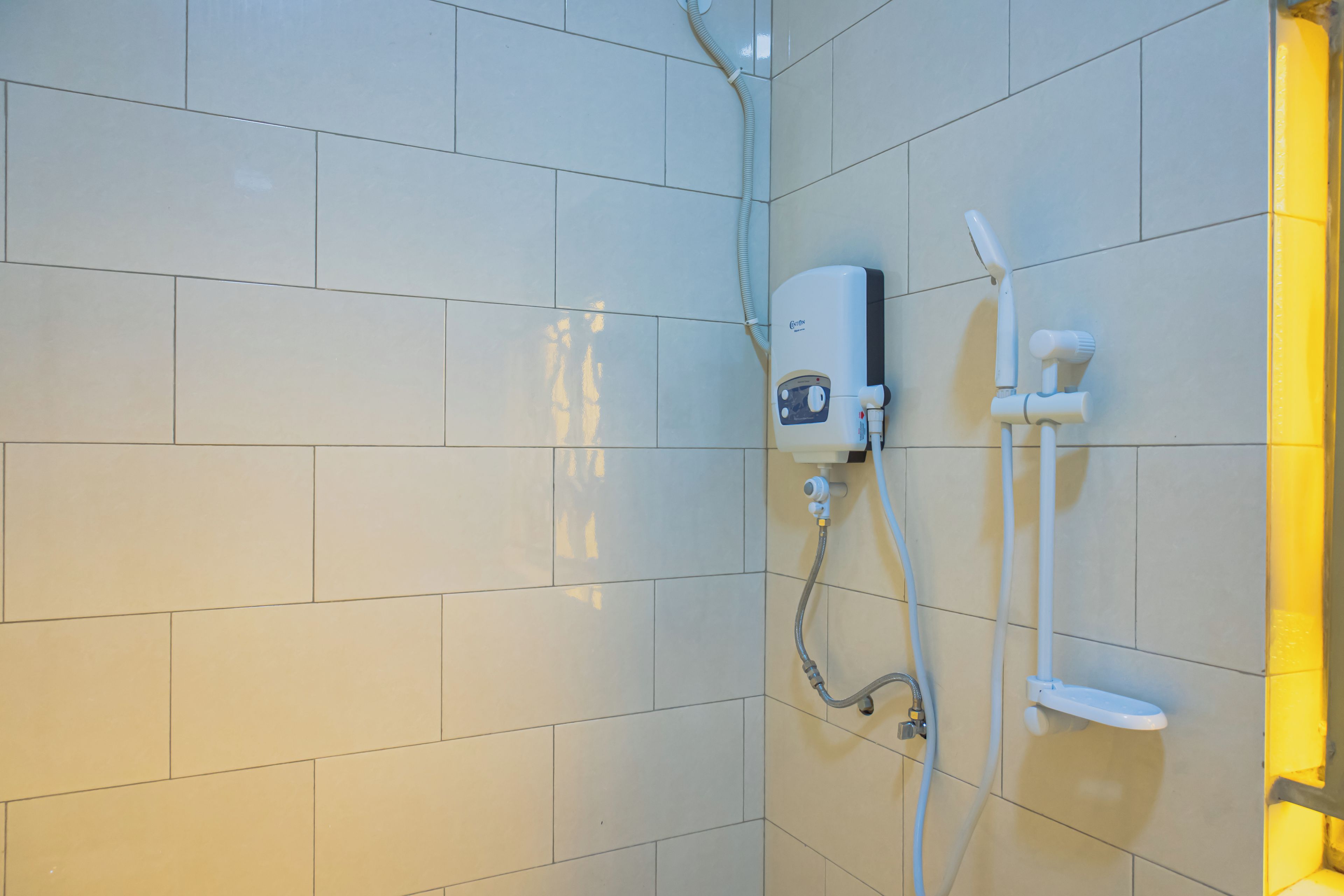 A shower area with a handheld showerhead, a wall-mounted control panel, and a handheld shower hose.