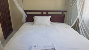 Ein Einzelbett mit weißer Bettdecke und Kissen, ein hölzernes Kopfholz und ein Fenster mit durchsichtigen Vorhängen.