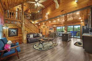 A spacious wooden cabin with a dining area, a living room with a sofa and coffee table, and a kitchen with a refrigerator. - Sleeps 12, Private Indoor Pool, Hot Tub, Theater, Arcade, 6 Mi to Dollywood (Pigeon Forge)