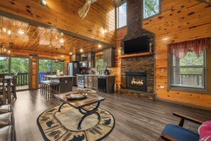 A spacious wooden cabin interior with a kitchen, dining area, and a fireplace. - Sleeps 12, Private Indoor Pool, Hot Tub, Theater, Arcade, 6 Mi to Dollywood (Pigeon Forge)