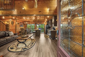A spacious living area with a wooden ceiling, a dining table, and a large window with decorative glass. - Sleeps 12, Private Indoor Pool, Hot Tub, Theater, Arcade, 6 Mi to Dollywood (Pigeon Forge)