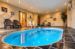 Une piscine intérieure avec un sol carrelé, entourée de chaises et agrémentée d’une plante en pot.