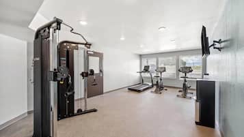 Une salle de sport équipée de matériel d’exercice, d’un tapis de course et d’un téléviseur fixé au mur.