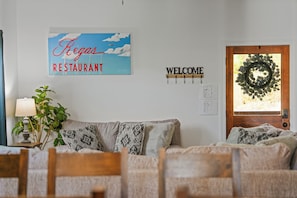 A living room with a couch, a lamp, a wall sign reading 'Regas Restaurant', a 'Welcome' sign, and a wreath on the door. - Sleeps 10, King Bed in Every Room, Hot Tub, Views, 3 Mi to Downtown Gatlinburg (Gatlinburg)
