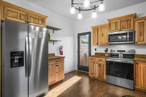 A kitchen with wooden cabinets, stainless steel appliances, a water dispenser, and a chandelier. - Sleeps 10, King Bed in Every Room, Hot Tub, Views, 3 Mi to Downtown Gatlinburg (Gatlinburg)