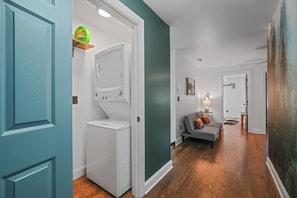 A laundry room with a washing machine and dryer, a shelf with a detergent bottle, and a hallway leading to a living area with a couch and a lamp. - Sleeps 10, King Bed in Every Room, Hot Tub, Views, 3 Mi to Downtown Gatlinburg (Gatlinburg)