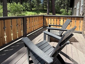 Um deck de madeira com cadeiras Adirondack e guarda-corpo de metal.