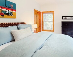 Un dormitorio con cama, ventana, lámpara y un cuadro en la pared.