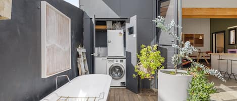 A compact outdoor laundry area with a washing machine, a drying rack, and potted plants.