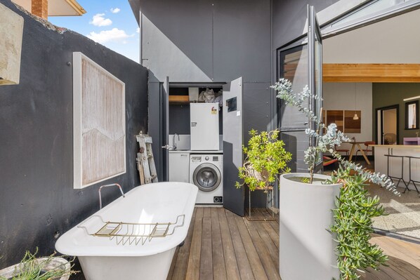 A compact outdoor laundry area with a washing machine, a drying rack, and potted plants.