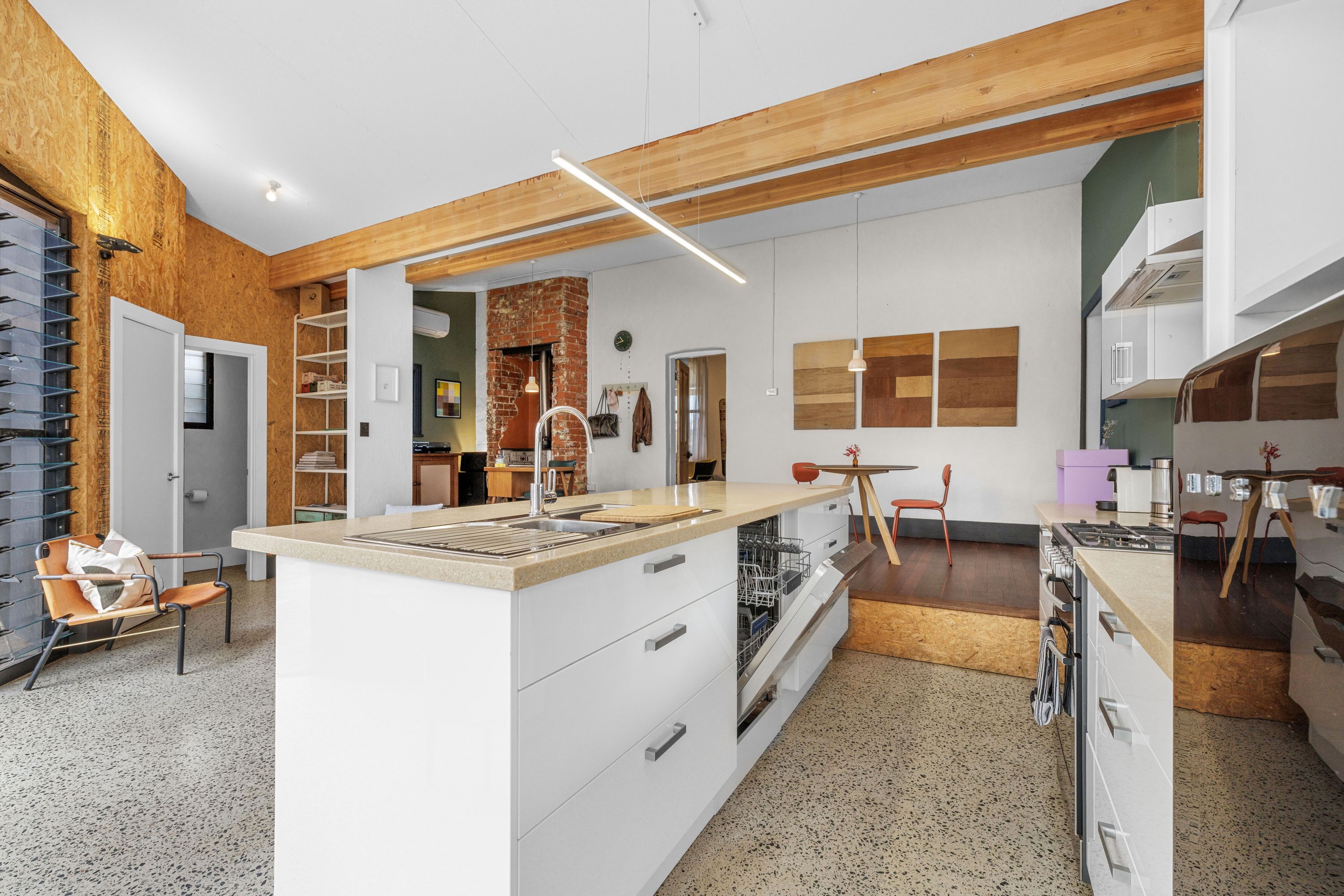 Una cocina moderna con una isla central, vigas de madera en el techo y un comedor con mesa y sillas.