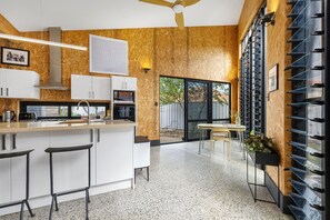 A modern kitchen with a central island, bar stools, a dining area with a table and chairs, and a large window with a view of the outdoors. - Heritage Haven - A Sepal Stay (Perth)