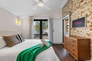A bedroom with a bed, a wooden dresser, a ceiling fan, a wall-mounted light, and a door leading to an outdoor area.