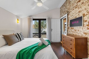 Un dormitorio con una cama, un tocador de madera, un ventilador de techo, una lámpara de pared y una puerta que da a un espacio exterior.
