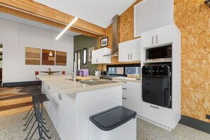 A modern kitchen with white cabinetry, a central island, and a built-in oven. - Heritage Haven - A Sepal Stay (Perth)