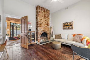 Una sala de estar con chimenea de ladrillo, un sofá, un armario de madera y un comedor con mesa y sillas.