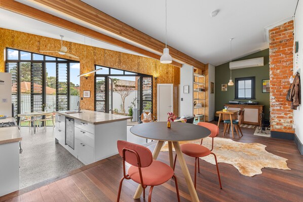 A modern kitchen with a central island, wooden beams, large windows, and a dining area with chairs. - Heritage Haven - A Sepal Stay (Perth)