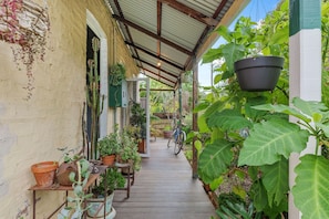 A covered outdoor area with a wooden floor, potted plants, and a bicycle. - Heritage Haven - A Sepal Stay (Perth)