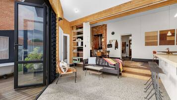 A modern interior with a glass door entrance, a seating area with a sofa and chairs, a kitchen with a dining table, and a wooden ceiling.