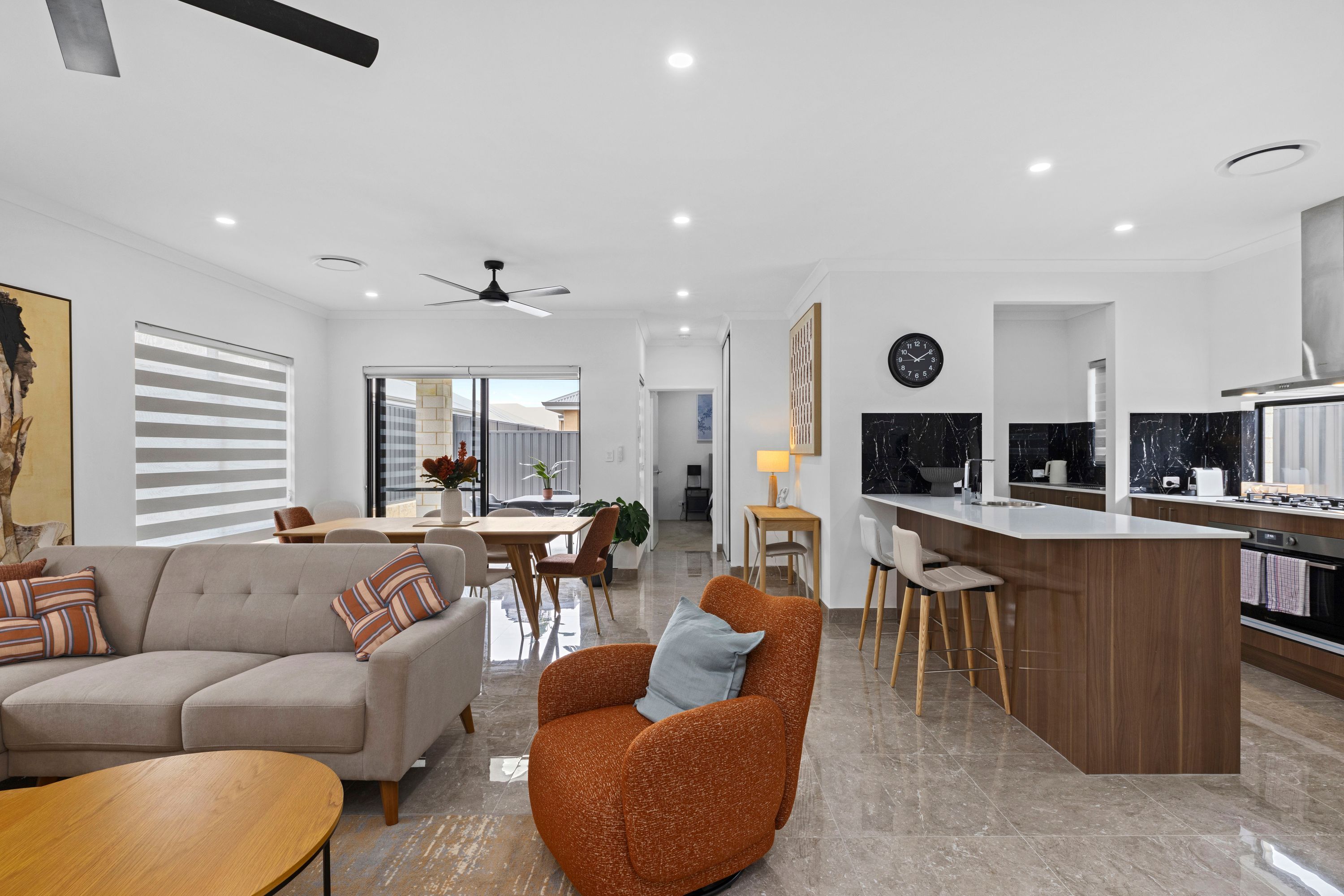 Un espacio habitable moderno con sofá, sillón, comedor, cocina y ventilador de techo.