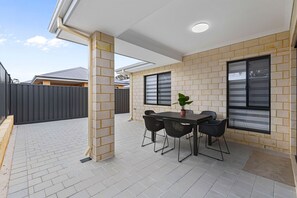 An outdoor patio with a table and chairs, a potted plant, and a view of a residential area. - Linger Laugh - A Sepal Stay (Henley Brook)