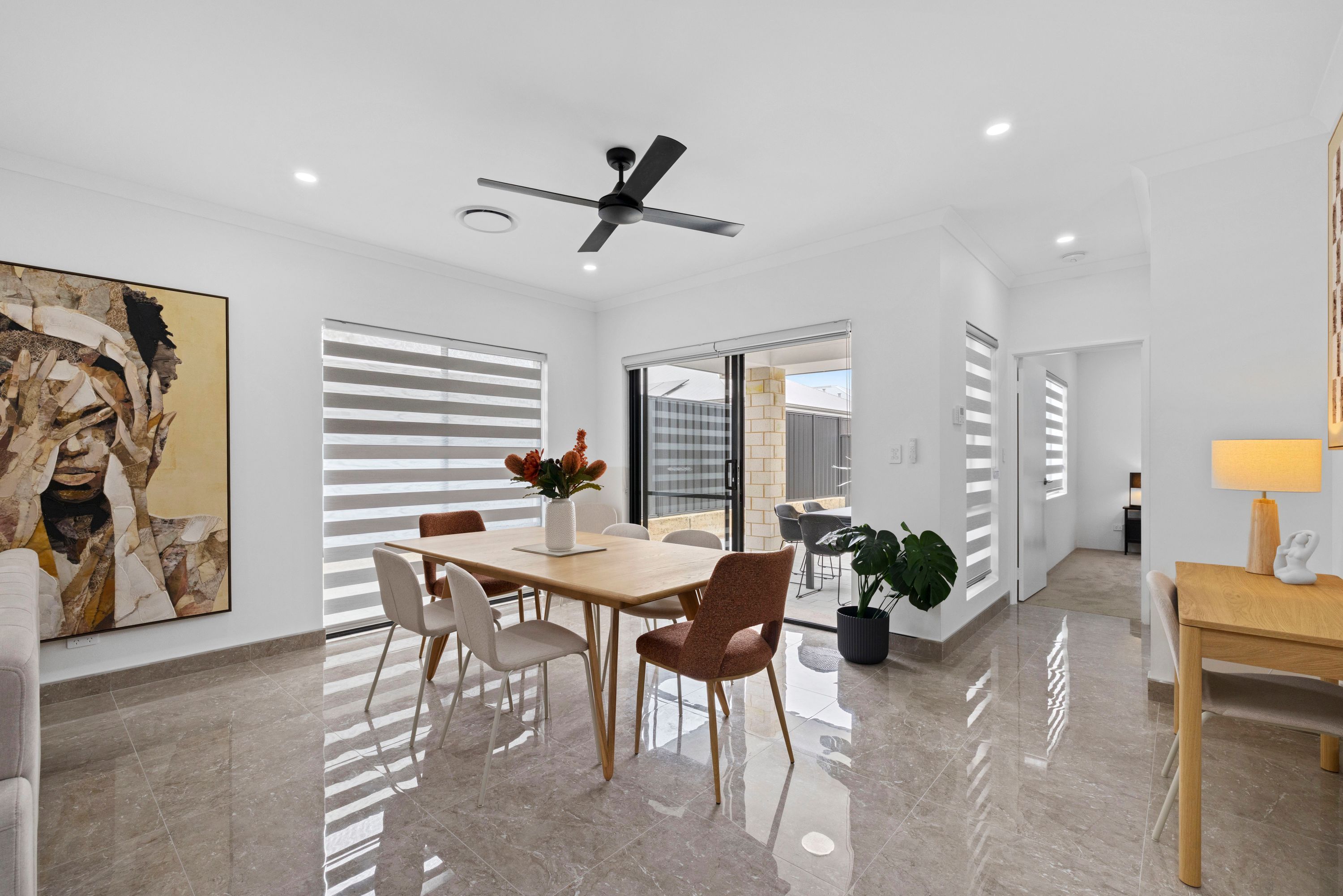 Un comedor moderno con ventilador de techo, una mesa de comedor con sillas y un cuadro grande en la pared.