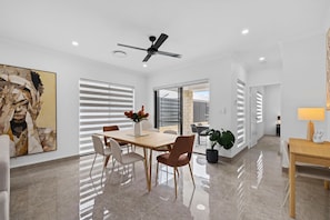 A modern dining area with a ceiling fan, a dining table with chairs, and a large painting on the wall. - Linger Laugh - A Sepal Stay (Henley Brook)
