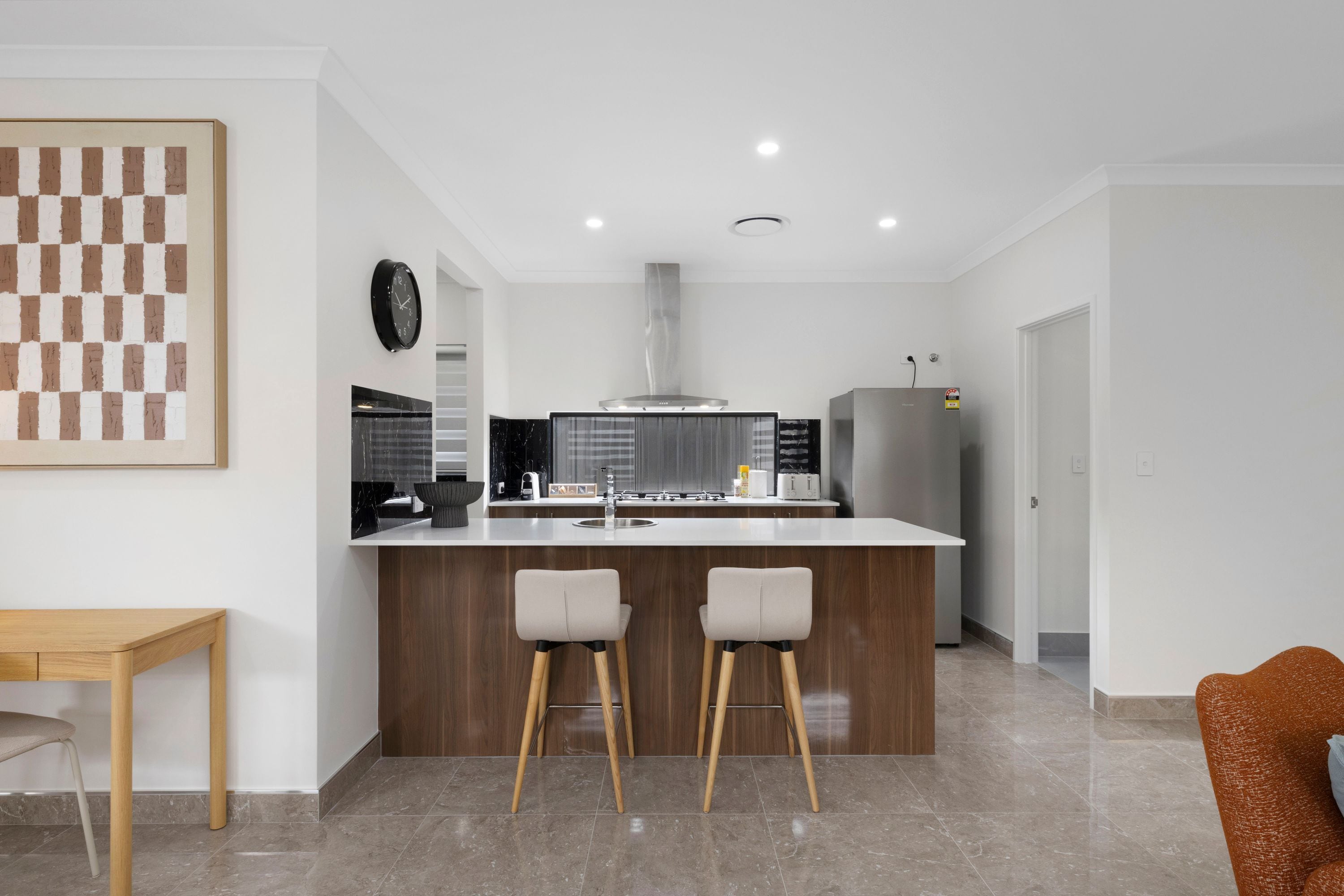 Cocina moderna con una isla central, dos taburetes de bar, una mesa de madera y un cuadro mural a cuadros.