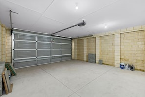 A garage with a closed metal door, a ceiling-mounted light fixture, and a brick wall. - Linger Laugh - A Sepal Stay (Henley Brook)