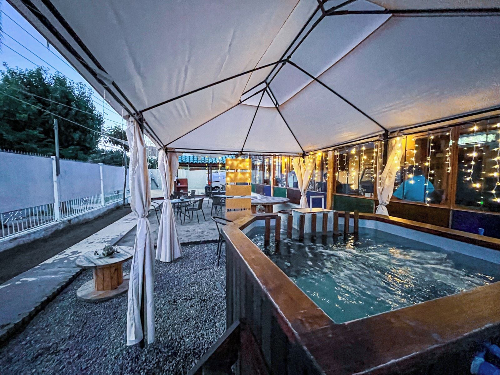Un espace extérieur aménagé avec des tables et des chaises, protégé par un grand parasol, et offrant une vue sur une piscine.