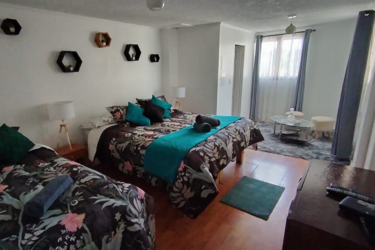 Habitación con dos camas, un escritorio y una silla. Decoración de pared hexagonal y ventana con cortinas.