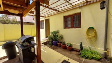 A covered patio area with a grill, potted plants, and a hose.