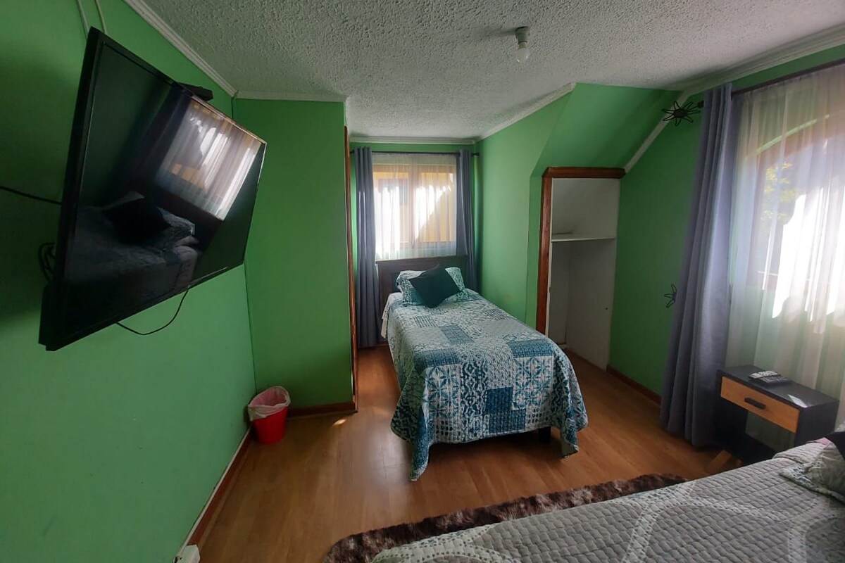 Una habitación con una cama, un televisor montado en la pared, una ventana con cortinas y una puerta.