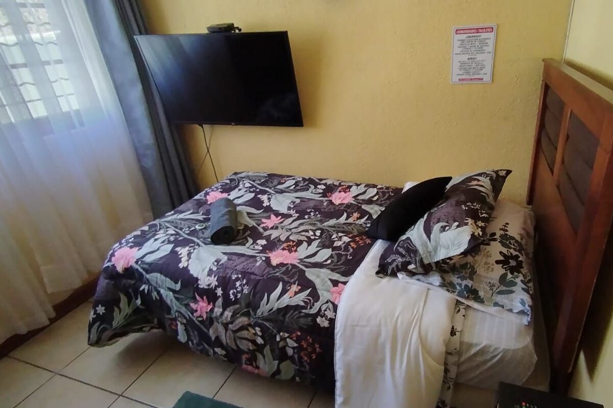 Una habitación pequeña con una cama, un televisor montado en la pared y un aviso en la pared.
