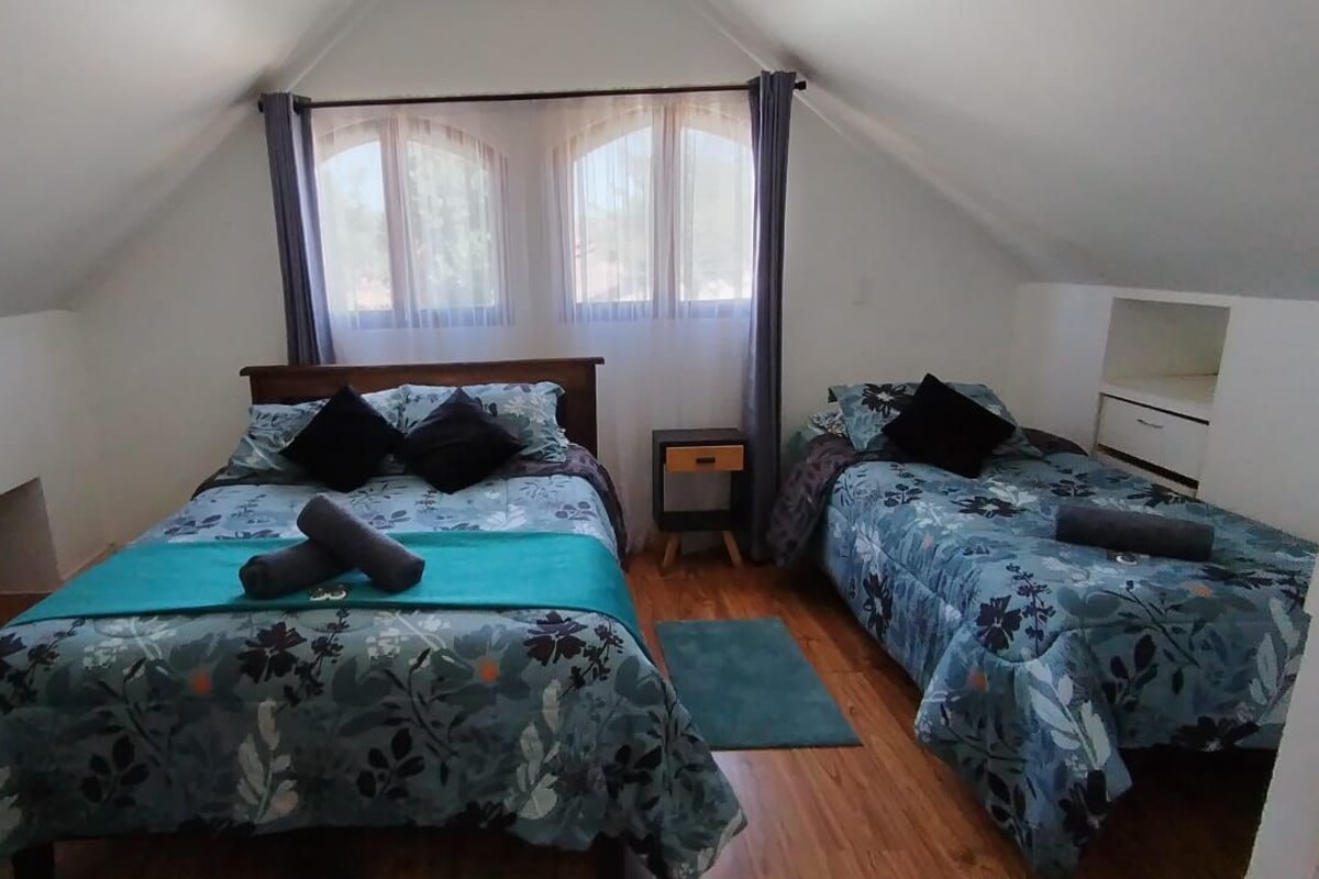 Un dormitorio con dos camas, una ventana con cortinas, una mesita de noche y un estante pequeño.