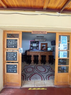 Entrada de hotel con marco de madera, un letrero de bienvenida y varios letreros de pizarra que enumeran servicios y comodidades.